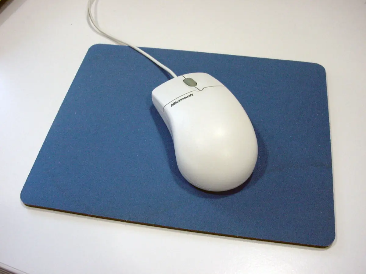 Visão superior de um mouse mecânico bege da Microsoft dos anos 90 sobre um mousepad de pano azul.